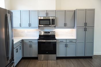 A kitchen with stainless steel appliances, gray cabinets, and backsplash at West Row Lofts and Townhomes in Birmingham, AL.